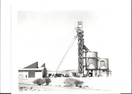Black-and-white photograph of the Whenan Shaft at the Olympic Dam mine site, showing the towering mining structure, adjacent silos, and nearby buildings, surrounded by a sparse outback landscape.